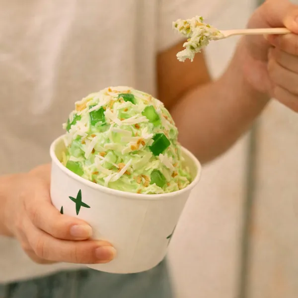 A cup of green gelato with jelly bits and a wooden spoon