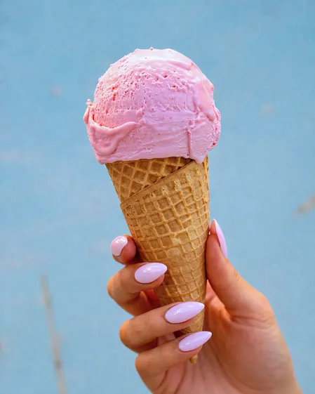 A pink scoop on a cone, held against a blue wall
